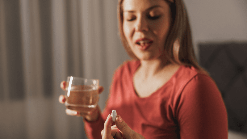 A woman taking a capsule with water before bed