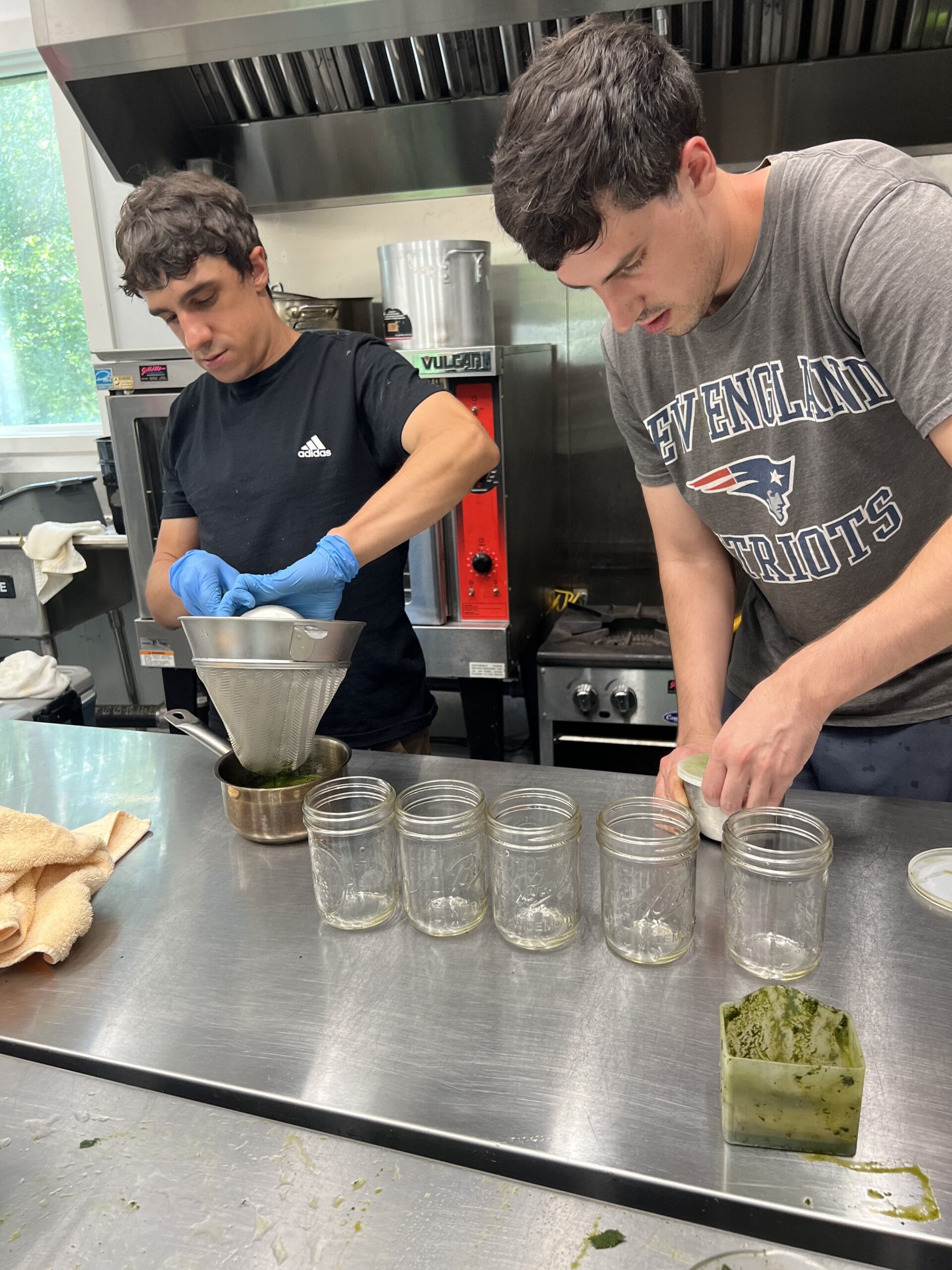 Two people preparing fresh hemp juice in a kitchen with jars and pressed green plant material